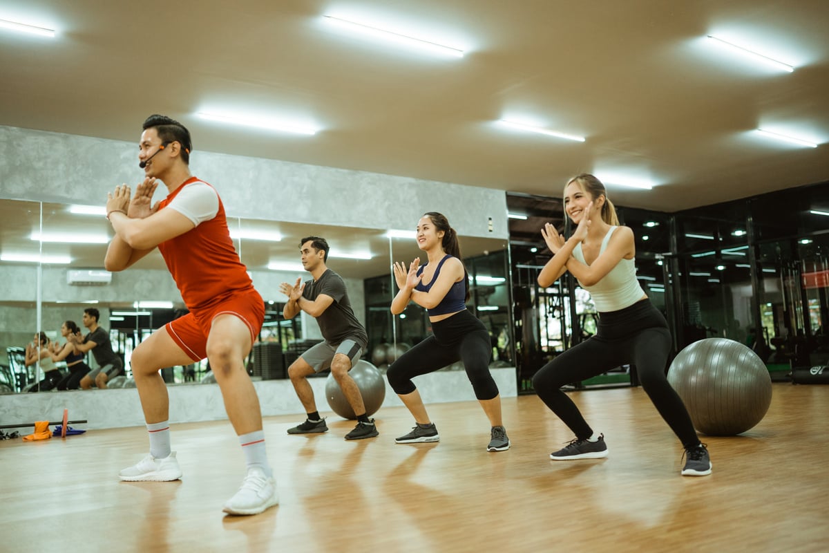 male instructor doing squats together with body combat participa